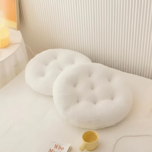 Two round white cushions on a bed with a yellow mug and book in a cozy room.
